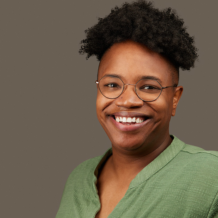 headshot Jessica right side of the frame with glasses and a green top on a gray background by M Carter Photography